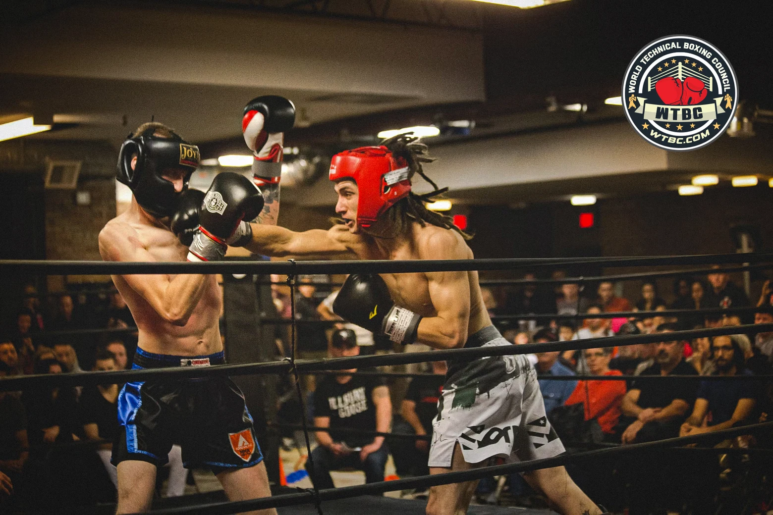 Two fighters in headgear, arena crowd behind